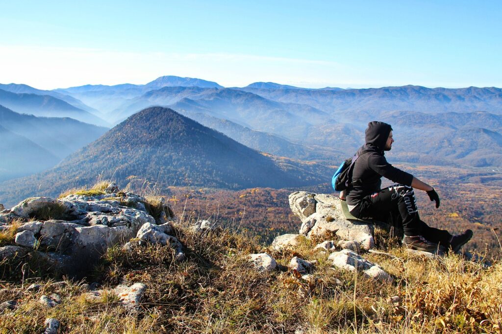 Hiking man sitting on a mountain with scenic view of mountain ranges in the background.